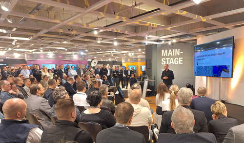 Großes Fachpublikum verfolgt aufmerksam einen Vortrag zur neuen KI-Technologie auf der Main Stage einer Messe, während der Referent vor einer Präsentationsleinwand spricht