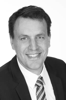 Lächelnder Mann im Anzug mit gestreifter Krawatte in einem professionellen Schwarz-Weiß-Porträt vor hellem Hintergrund