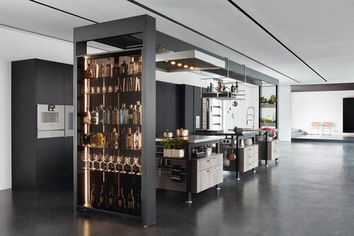 Offene Designerküche mit zentraler Kochinsel, beleuchtetem Getränkeregal und modernem Edelstahlherd in einem großzügigen, minimalistischen Loftraum