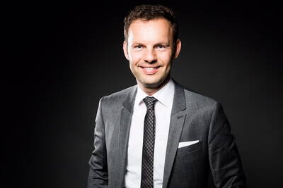 Lächelnder Mann im grauen Anzug mit Krawatte vor dunklem Hintergrund in professioneller Porträtaufnahme