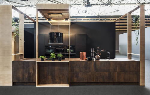 Moderne Kochinsel aus dunklem Holz mit hängender Dunstabzugshaube, Kräutertöpfen und Deko-Vasen in einer offen gestalteten Designküche vor schwarzer Rückwand