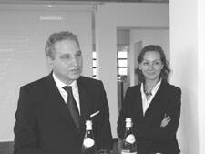 Zwei elegant gekleidete Personen stehen in einem modernen Konferenzraum nebeneinander und unterhalten sich, vor ihnen stehen Wasserflaschen auf einem Tisch.