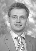 Junger Mann mit Brille im Anzug und gestreifter Krawatte vor unscharfem Studiohintergrund