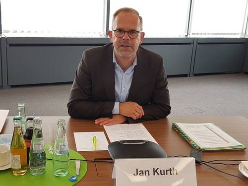 Mann im Anzug sitzt an einem Konferenztisch vor Unterlagen und Getränkeflaschen in einem modernen Besprechungsraum