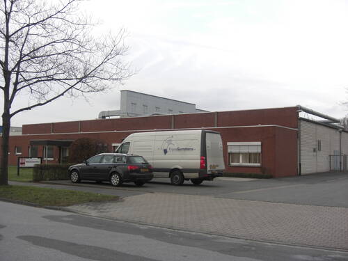 Lieferwagen und Kombi parken vor einem flachen Backsteingebäude in einem Gewerbegebiet an einem grauen, bewölkten Tag