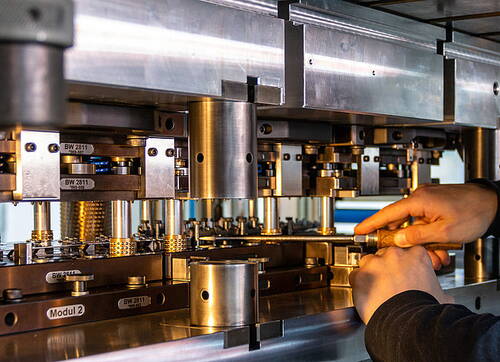Techniker justiert mit beiden Händen eine komplexe Metallstanzmaschine in einer industriellen Werkhalle