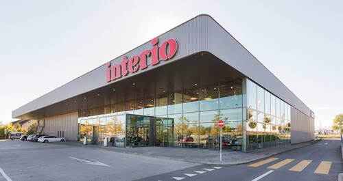 Modernes Möbelhaus mit großer Glasfassade, rotem „interio“-Schriftzug und Parkplatz im Vordergrund