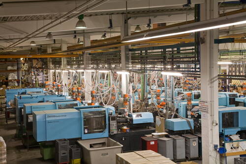 Reihe automatisierter Spritzgussmaschinen in einer hell beleuchteten Industriehalle mit zahlreichen Schläuchen, Steuerpulten und Materialbehältern