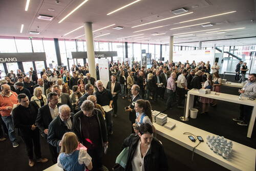 Große Menschenmenge wartet im Foyer einer Messehalle an mehreren Anmeldeschaltern, während Mitarbeiter in Tracht Besucher registrieren und Infomaterial ausgeben