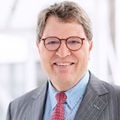 Mittelalterlicher Mann mit Brille und grauem Anzug lächelt in einer hellen, modernen Büroumgebung in die Kamera