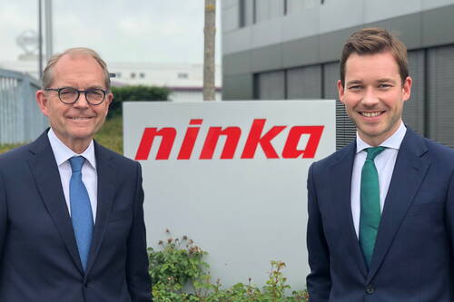 Zwei lächelnde Männer im Businessanzug stehen vor dem Firmengebäude von Ninka neben einem großen Firmenschild mit rotem Logo