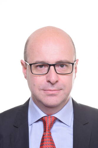 Kahlköpfiger Mann mit schwarzer Brille und roter Krawatte im Anzug blickt neutral in die Kamera vor weißem Hintergrund