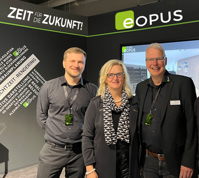 Drei lächelnde Messemitarbeitende posieren vor einem schwarzen eOPUS‑Messestand mit dem Slogan „Zeit für die Zukunft“ und technischer Schlagwortwand im Hintergrund.