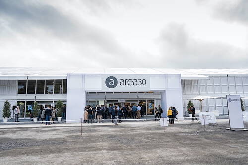 Besuchergruppen versammeln sich vor dem Haupteingang der Messehalle „area30“ unter bewölktem Himmel.