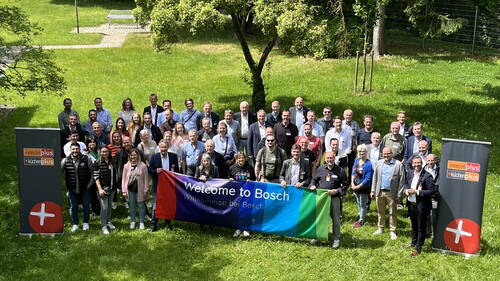Gruppe von Teilnehmenden einer electroplus und küchenplus Veranstaltung hält im Grünen ein großes, buntes „Welcome to Bosch“-Banner zwischen zwei Marken-Roll-ups hoch.
