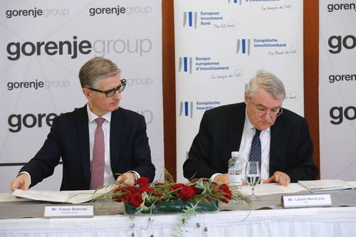 Zwei Geschäftsleute unterzeichnen an einem Tisch mit Blumenarrangement einen offiziellen Vertrag vor Bannern der Gorenje Group und der Europäischen Investitionsbank.