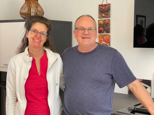 Lächelndes Paar steht entspannt nebeneinander in einer modernen Küche mit Gewürzbild an der Wand.