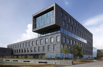Moderner Bürokomplex aus dunklem Klinker mit großen Glasfronten und auskragendem Obergeschoss an einer begrünten Straße