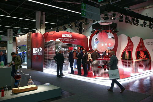 Messestand von AKP mit rot-weiß beleuchtetem Design, mehreren Besuchern im Gespräch und modernen Arbeitsplatten- und Nischenpräsentationen in einer Messehalle