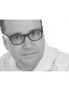 Porträt eines nachdenklich blickenden Mannes mit dunkler Brille und weißem Hemd vor hellem Hintergrund