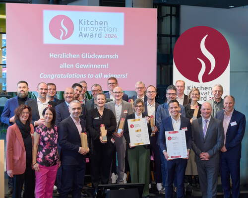 Gruppe von Preisträgern steht lächelnd mit Urkunden und Trophäen auf einer Bühne vor dem Schriftzug „Kitchen Innovation Award 2024“ und einem Glückwunschbanner in Deutsch und Englisch