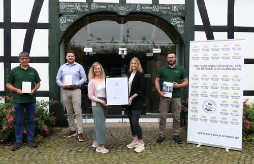 Fünf Personen stehen vor einem Fachwerkgebäude und präsentieren stolz eine große Auszeichnungsurkunde sowie Plaketten für das Gütesiegel „Best Place to Learn“ in der betrieblichen Ausbildung.