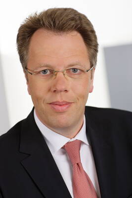Mittelalterlicher Mann mit Brille im Business-Anzug und roter Krawatte blickt direkt und freundlich in die Kamera vor hellem Hintergrund