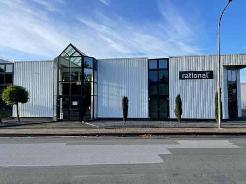 Moderne weiße Industriehalle mit großer verglaster Eingangsfassade und rational‑Firmenlogo an der Straßenseite bei klarem Himmel