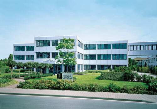 Modernes Büro- und Verwaltungsgebäude von Westag & Getalit AG mit großer Glasfassade, gepflegtem Vorgarten und Zufahrt an einer ruhigen Straße.