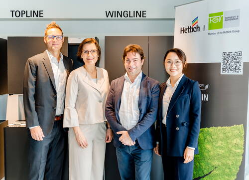 Vier Geschäftsleute posieren lächelnd im Showroom vor den Produktbezeichnungen „Topline“ und „Wingline“ sowie einem Hettich- und FGV-Markenbanner.