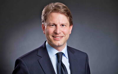 Lächelnder Mann im dunklen Anzug mit Krawatte vor neutral grauem Hintergrund