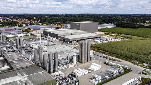 Großes Industrie- und Logistikgelände mit mehreren Hallen, hohen Edelstahlsilos und Lagerflächen am Rand eines landwirtschaftlich geprägten Gebiets neben einem Dorf.