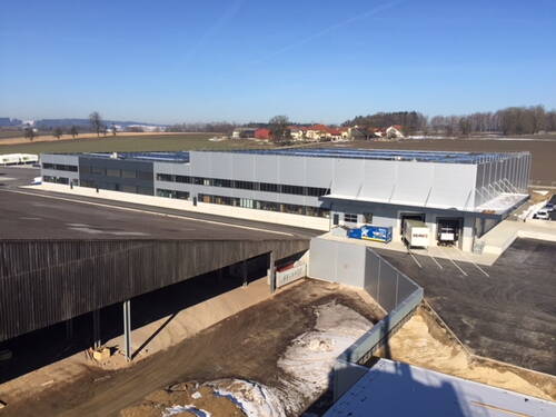 Modernes Industrie- und Logistikgebäude mit großflächigem Parkplatz in ländlicher Umgebung an einem sonnigen Wintertag