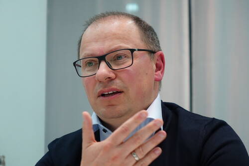 Mittelalterlicher Mann mit Brille spricht gestikulierend in einem hellen Raum und wirkt konzentriert