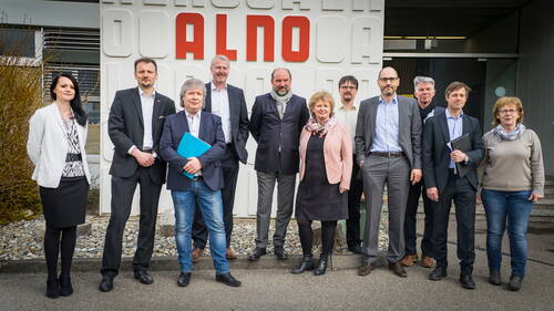 Gruppe von Geschäftsleuten und Angestellten posiert in formeller Kleidung vor dem Gebäude des Unternehmens ALNO