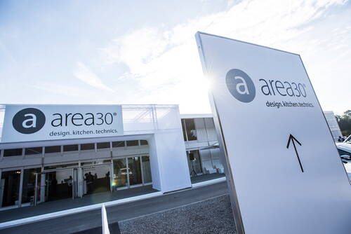 Großes, weißes Messegebäude der area30 mit prominentem Logo und Wegweiser-Schild im Vordergrund bei sonnigem Himmel