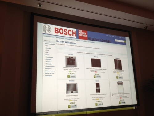 Beamerprojektion einer Bosch-Webseite, auf der verschiedene Einbauküchengeräte mit Bildern, Preisen und Produktdetails präsentiert werden