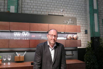 Mittelalter Mann mit Brille lächelt vor einer modernen Küchenzeile mit beleuchteten Gläsern und kupferfarbenen Dekokugeln in einer Industriehalle