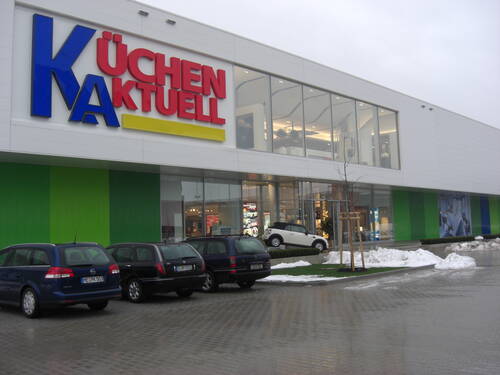 Großes Küchen Aktuell Einrichtungshaus mit verglaster Fassade, davor mehrere parkende Autos auf nassem Parkplatz an einem winterlichen Tag