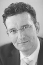 Mittelalterlicher Mann mit Brille und Anzug blickt nachdenklich in die Kamera