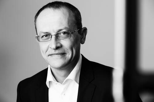 Mittelalterlicher Mann mit Brille im Anzug, der in einem schwarz-weißen Porträt freundlich in die Kamera lächelt