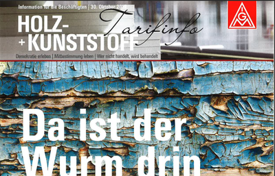 Titelblatt der IG‑Metall‑Tarifinfo „Holz + Kunststoff“ mit großem Schriftzug „Da ist der Wurm drin“ vor einer Nahaufnahme von rissigem, abgeplatztem blauen Lack auf verwittertem Holz