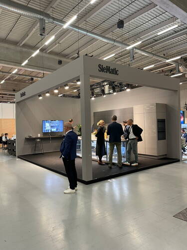 Modern gestalteter SieMatic-Messestand in einer Messehalle, an dem mehrere Besucher eine hochwertige, minimalistische Küchenausstellung betrachten und sich darüber austauschen.