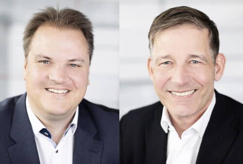 Zwei lächelnde Geschäftsmänner in Anzügen im professionellen Porträt vor hellem, unscharfem Hintergrund