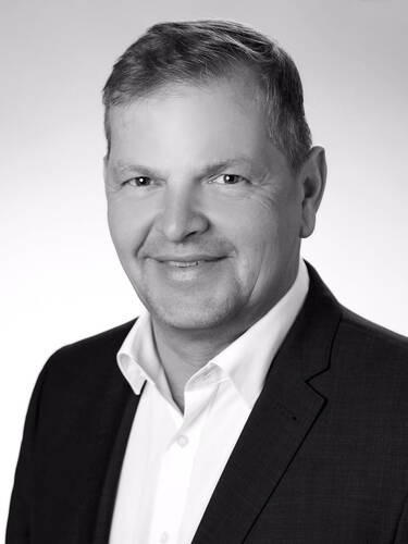 Freundlich lächelnder Mann mittleren Alters im Anzug vor hellem Studiohintergrund in einer professionellen Schwarz-Weiß-Porträtaufnahme
