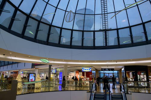 Einkaufszentrum mit verglaster Kuppel, Blick auf einen Wasserturm im Hintergrund, darunter weihnachtlich beleuchtete Dekoration, ein IKEA-Geschäft und Menschen auf der Ladenebene neben Rolltreppen