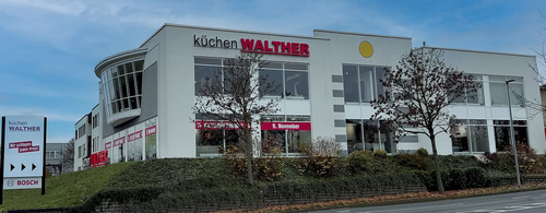 Modernes Küchenstudio-Gebäude von Küchen Walther mit großer Glasfassade, Werbebannern im Schaufenster und vorgelagerter Straße an einem klaren Herbsttag