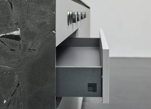 Geöffnete graue Küchenschublade in einer modernen Arbeitszeile mit dunkler Steinfront und Metallgriffen