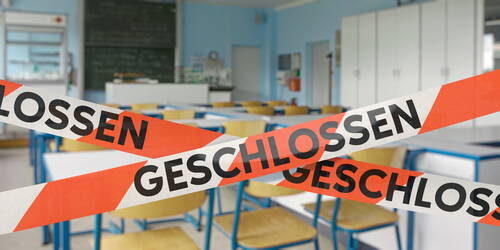 Leeres Klassenzimmer mit hochgestellten Stühlen, das mit rot-weißem Absperrband und der Aufschrift „geschlossen“ versperrt ist