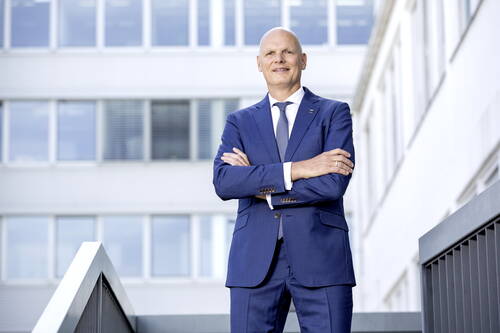 Selbstbewusster Geschäftsmann im blauen Anzug steht mit verschränkten Armen auf einer Außentreppe vor einem modernen Bürogebäude
